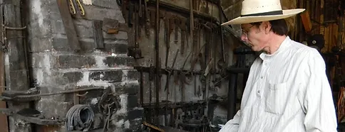 A man in a Summerfield hat is standing in front of a stove.