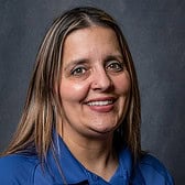 Headshot of Chrystal Porter, a smiling woman with long brown hair, wearing a blue shirt. The background is dark and uniform.